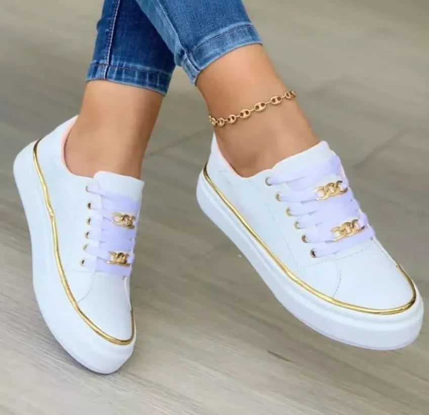White low-top sneakers with gold trim and chain accents, paired with skinny jeans.