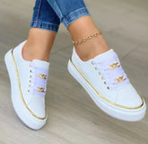 White low-top sneakers with gold trim and chain accents, paired with skinny jeans.
