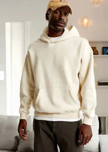 Man wearing an off-white oversized hoodie with front pocket and relaxed fit streetwear style