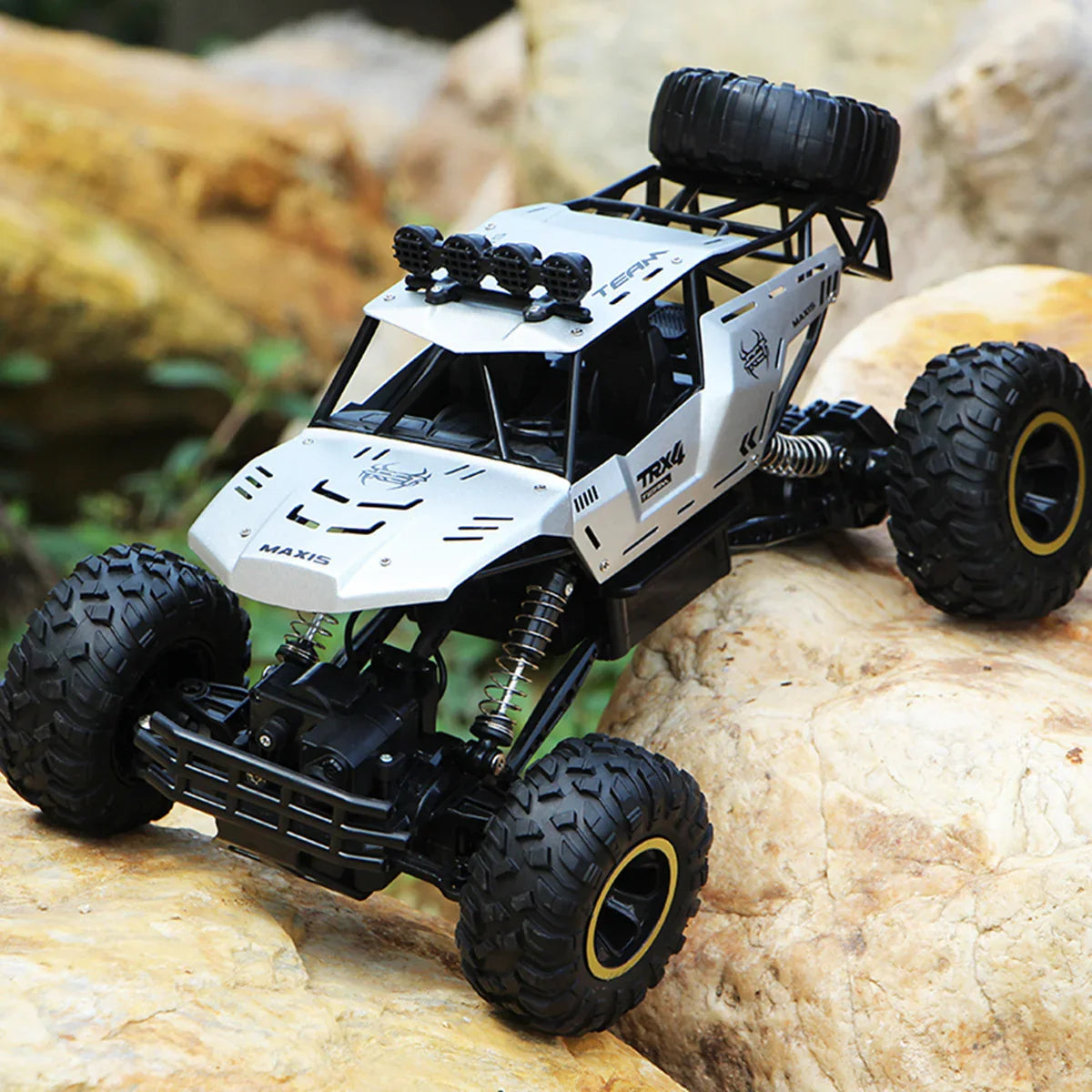 Silver off-road RC truck with large tires and rugged design on rocky terrain