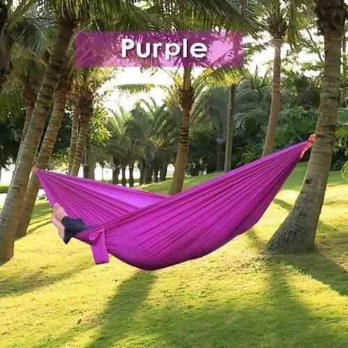 Lightweight purple hammock made of soft fabric, strung between palm trees outdoors.