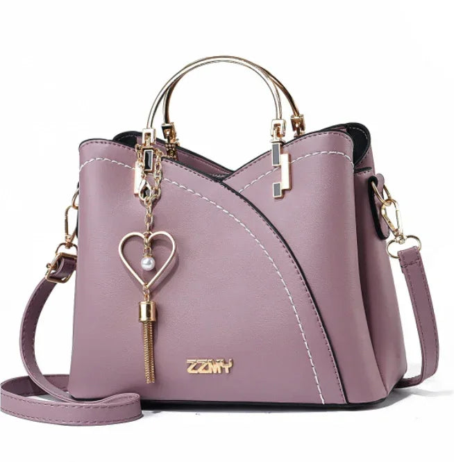 Lavender faux leather handbag with gold handles, heart charm, and crossbody strap, modern style