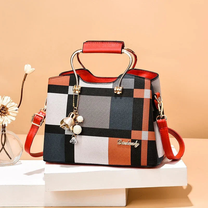 Plaid structured handbag with red leather accents, gold hardware, and charm accessory.