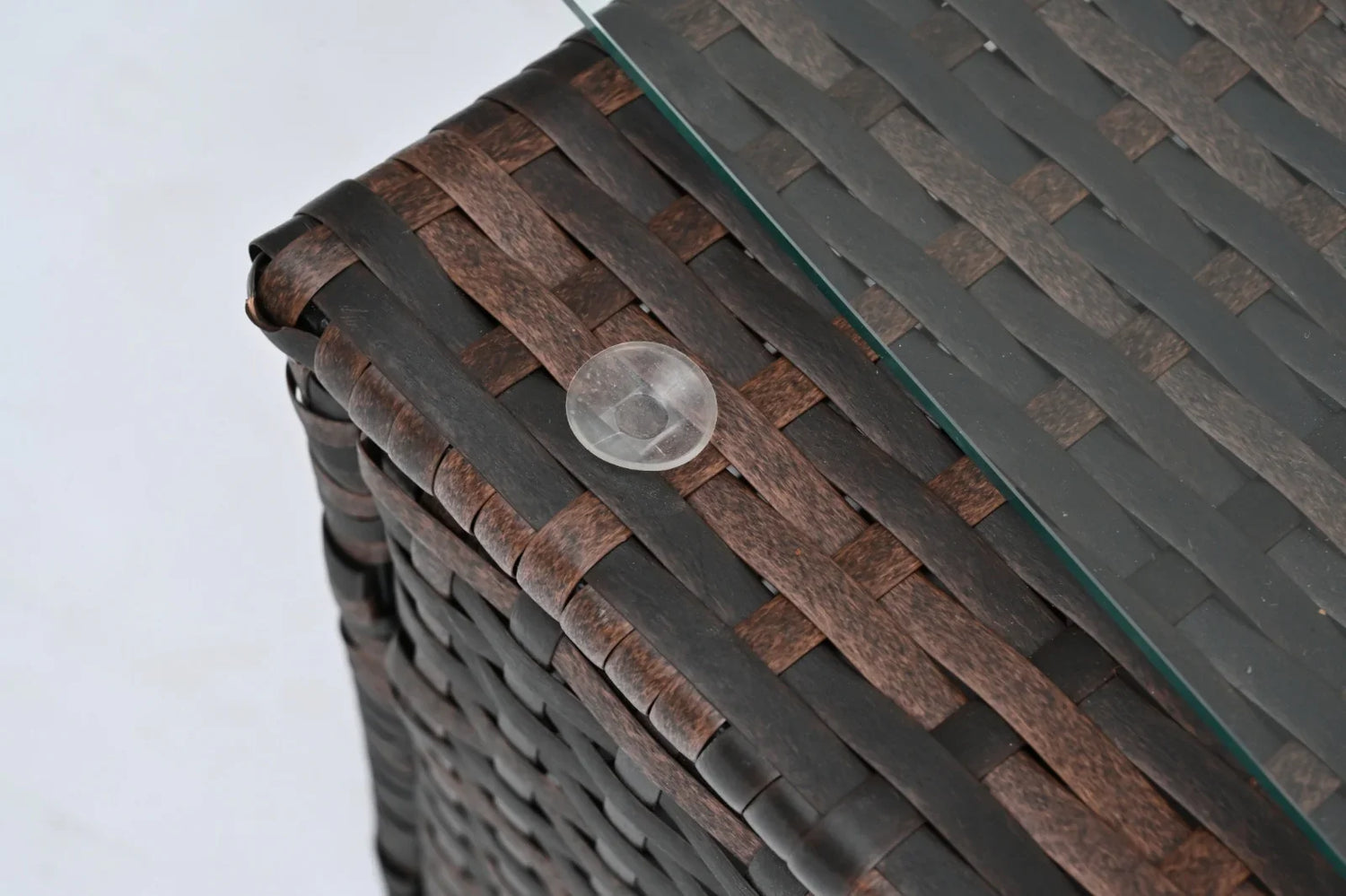 Close-up of brown woven rattan table corner with glass top and clear rubber pad