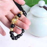 Hand holding black bead bracelet with gold accents and decorative gold charm