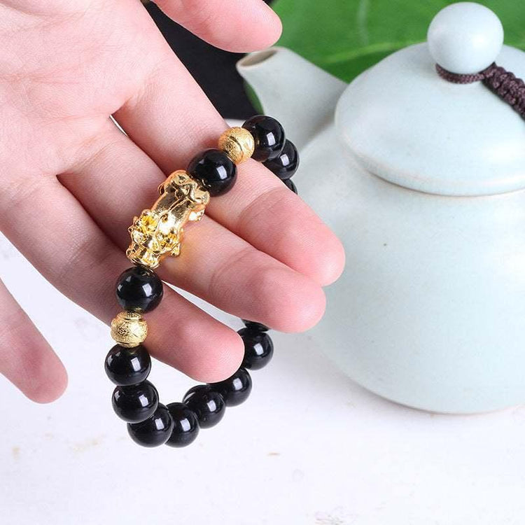 Hand holding black bead bracelet with gold accents and decorative gold charm