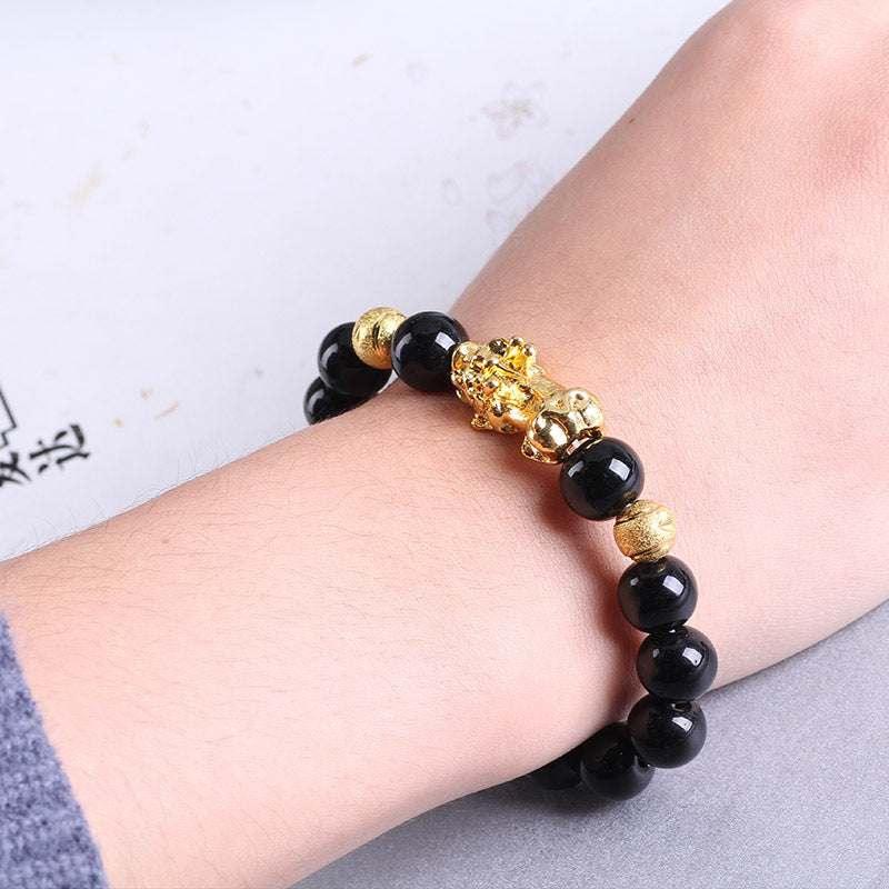 Black beaded bracelet with gold accents and lion charm, worn on wrist, modern streetwear style