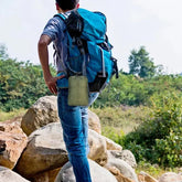 Man wearing blue outdoor jacket, jeans, and large blue hiking backpack standing on rocks outdoors