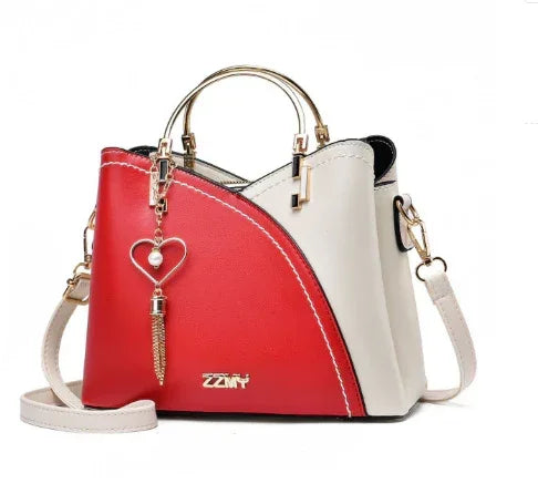 Colorblock handbag with red and beige panels, gold-tone handles, heart pendant, structured fit