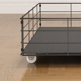 Black metal wire storage basket with textured base and wheels on wooden floor