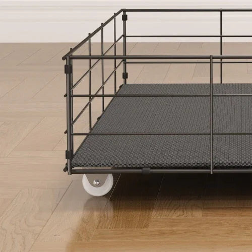 Black metal wire storage basket with textured base and wheels on wooden floor