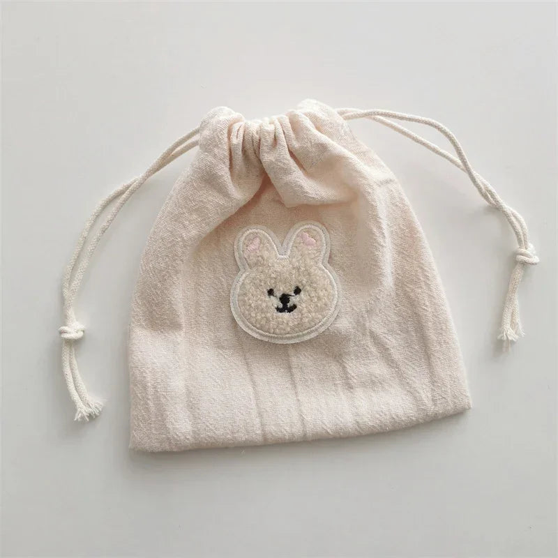 Beige cotton drawstring pouch with fuzzy bunny face patch, soft texture, casual style
