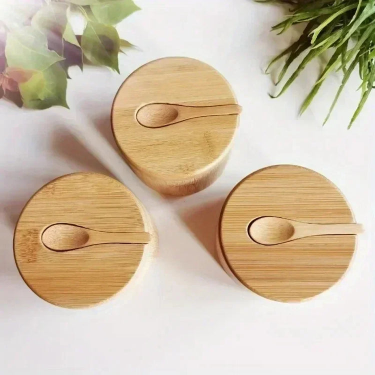 Three round bamboo storage containers with matching lids and spoons on a white surface