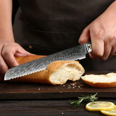 Person in a dark apron slicing bread with a textured steel serrated knife on a wooden board