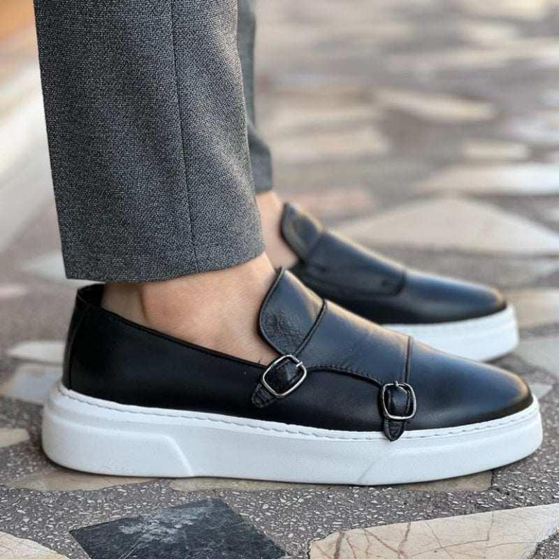 Black leather monk strap loafers with white chunky soles, paired with gray slim-fit pants