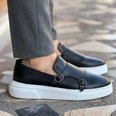 Black leather monk strap loafers with white chunky soles, paired with gray slim-fit pants