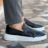 Black leather monk strap loafers with white chunky soles, paired with gray slim-fit pants