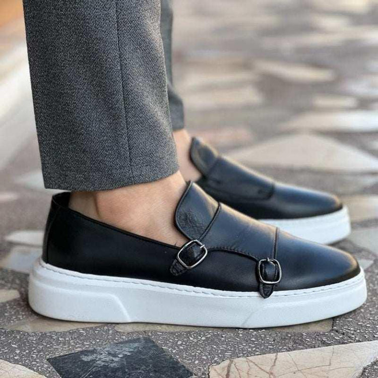 Black leather monk strap loafers with white chunky soles, paired with gray slim-fit pants