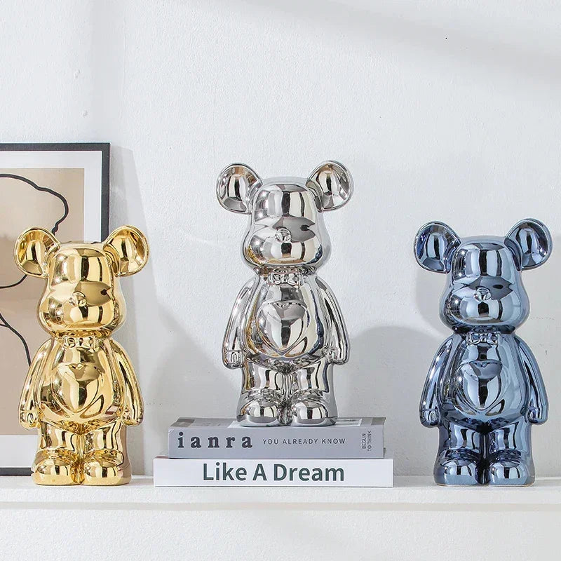 Three metallic bear figurines in gold, silver, and blue on a white shelf, modern decor style.