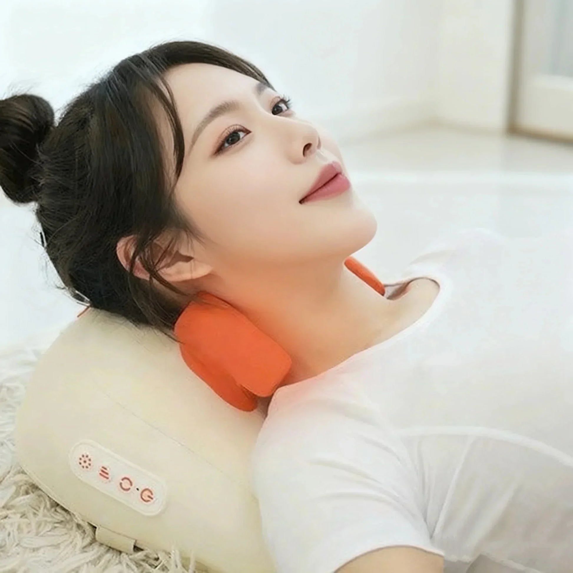 Woman in white fitted t-shirt using an orange and beige neck massager pillow indoors
