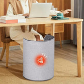 Woman in a beige long-sleeve dress and vest working at a desk, feet in a gray fabric foot warmer.