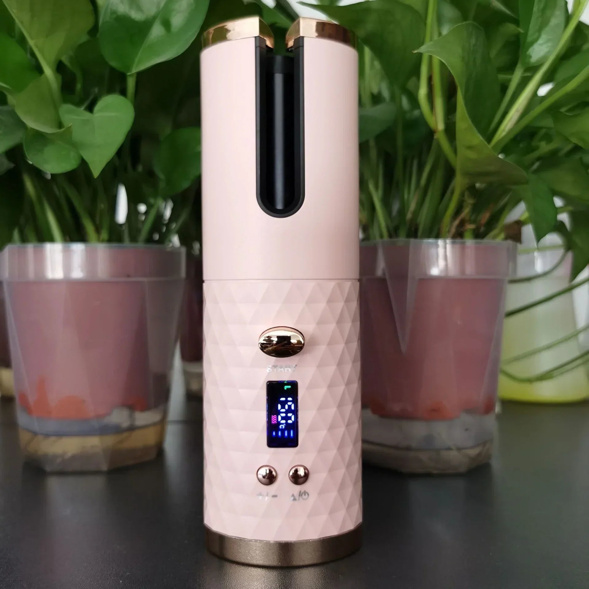 Pink and gold portable hair curler with digital display, geometric textured body, on black surface
