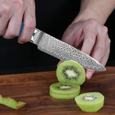 Person slicing fresh kiwi with a patterned stainless steel kitchen knife on a wooden board
