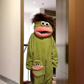 Person wearing oversized green plush hooded jumpsuit with cartoon face and large pink lips