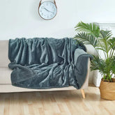Soft gray waterproof blanket draped over beige sofa in bright room with clock and plant