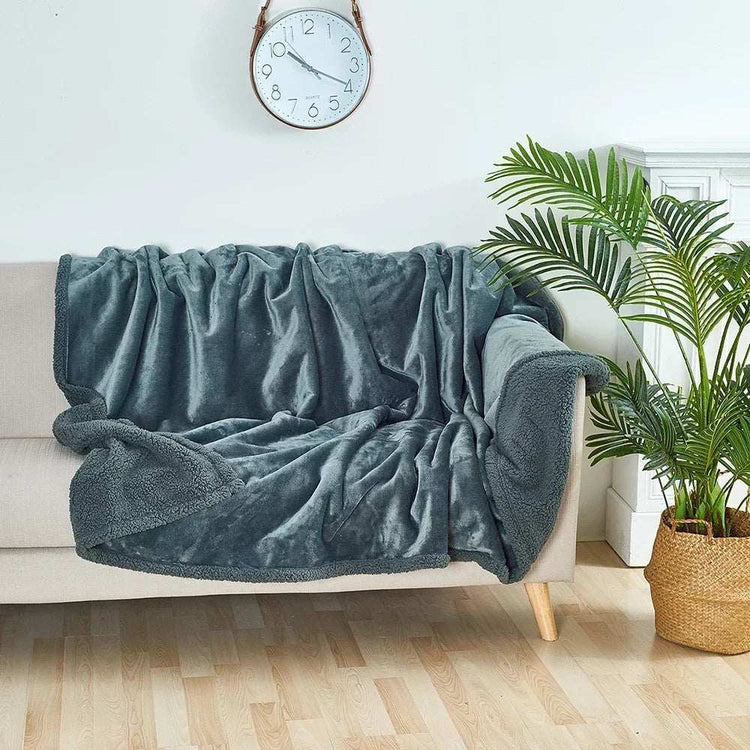 Soft gray waterproof blanket draped over beige sofa in bright room with clock and plant