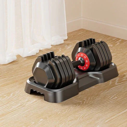 Adjustable black dumbbell with red weight dial on a wooden floor in a bright room