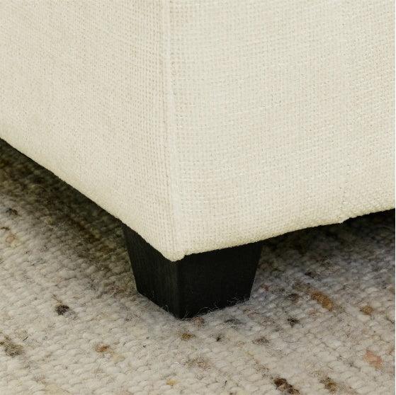 Close-up of cream textured fabric sofa with dark wood leg on a patterned carpet
