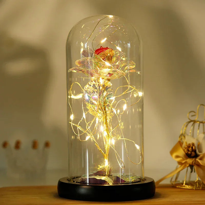 Iridescent artificial rose with gold stem and LED fairy lights in glass dome display