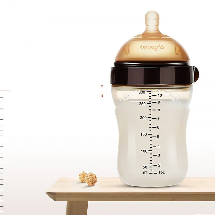 Translucent baby bottle with brown silicone nipple, measurement markings, and ergonomic shape on wooden table.