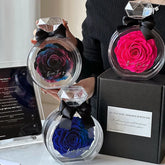 Woman in fitted black ribbed sweater holding colorful artificial roses in clear round cases with diamond-shaped tops and black bows.