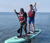 Two people paddleboarding in red life jackets, one in black leggings and the other in blue shorts.