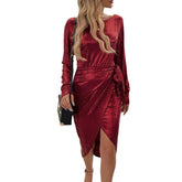 Woman wearing a shiny burgundy velvet long-sleeve wrap dress with side tie and slim fit
