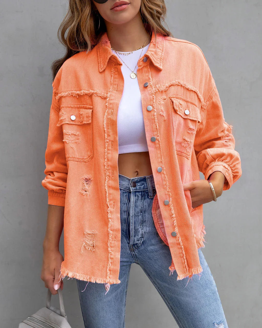 Woman wearing distressed orange denim jacket, white crop top, and blue skinny jeans