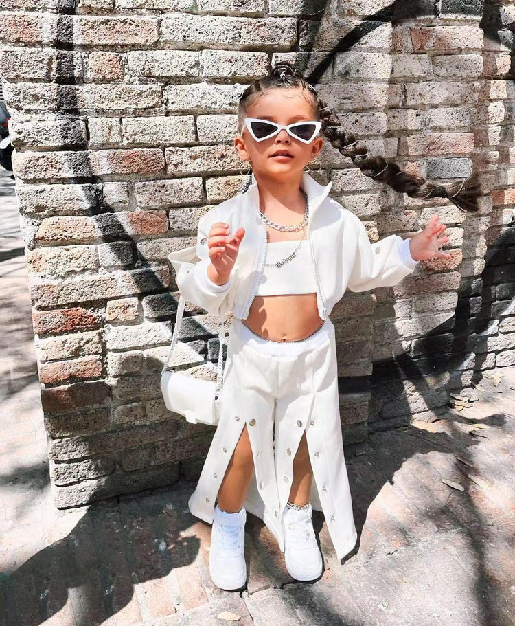 Child wearing white streetwear set with cropped jacket, wide-leg pants, and sneakers outdoors