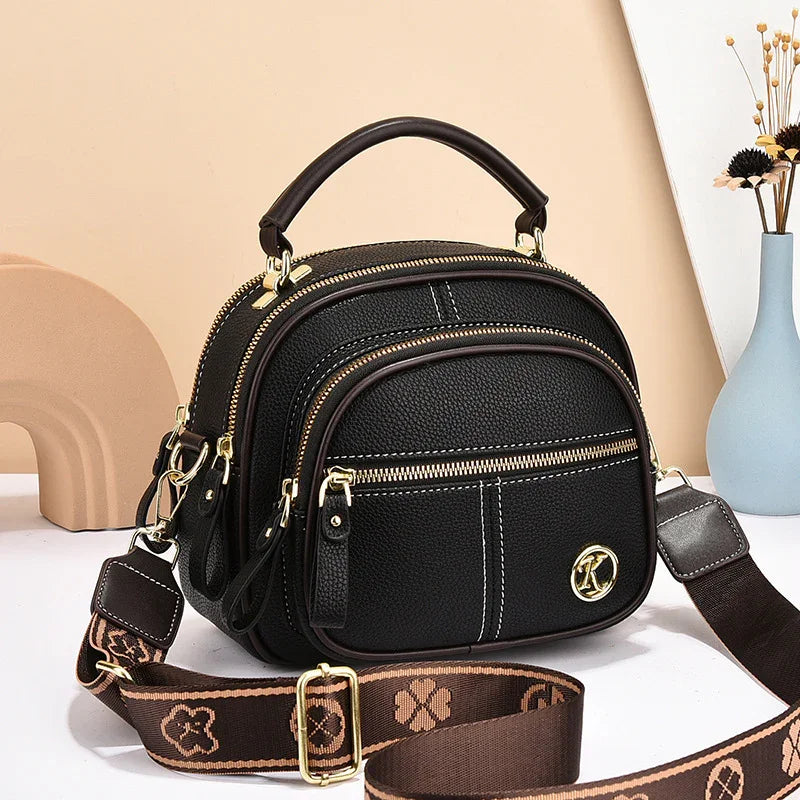 Black textured leather crossbody bag with gold zippers, adjustable strap, and top handle