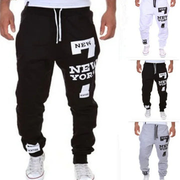 Men's streetwear jogger pants in black, white, and grey with bold New York graphic print, relaxed fit, drawstring waist.