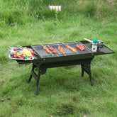 Outdoor portable charcoal grill with metal mesh top grilling skewers, set on grass