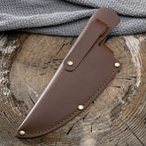 Brown leather knife sheath with brass rivets on rustic wooden surface