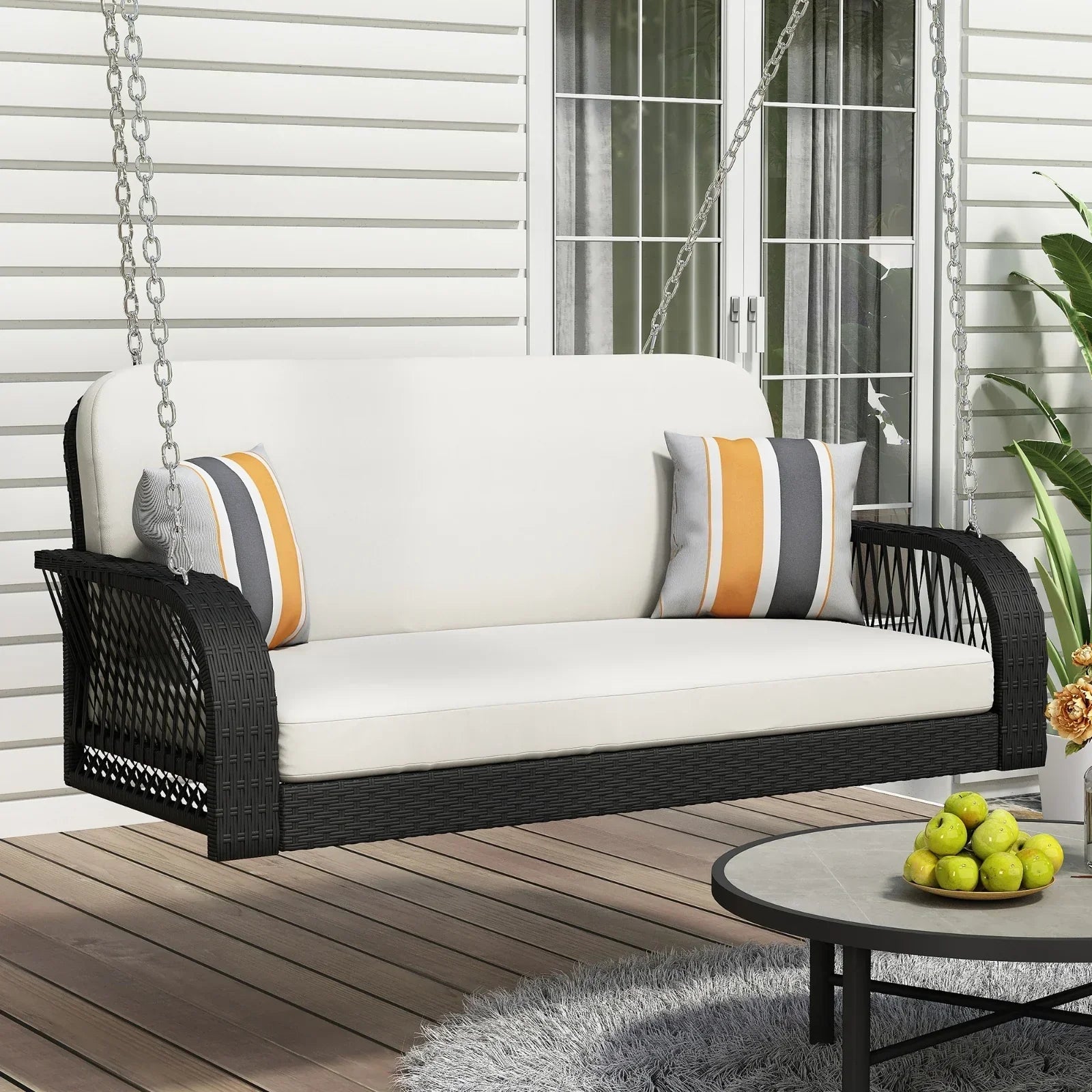 Outdoor patio swing with black wicker frame, white cushions, and striped accent pillows