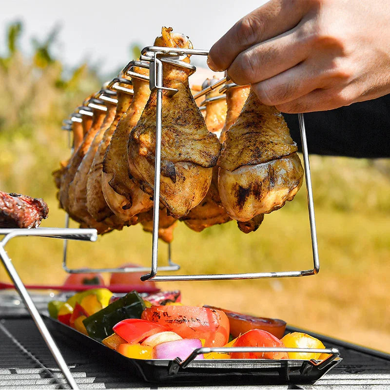 Grilled chicken drumsticks hanging on a metal rack over colorful grilled vegetables outdoors