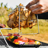 Grilled chicken drumsticks hanging on a metal rack over colorful grilled vegetables outdoors