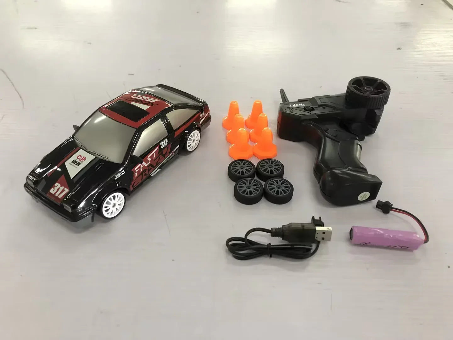 Remote control drift car set with black and red car, extra wheels, cones, and accessories on table.