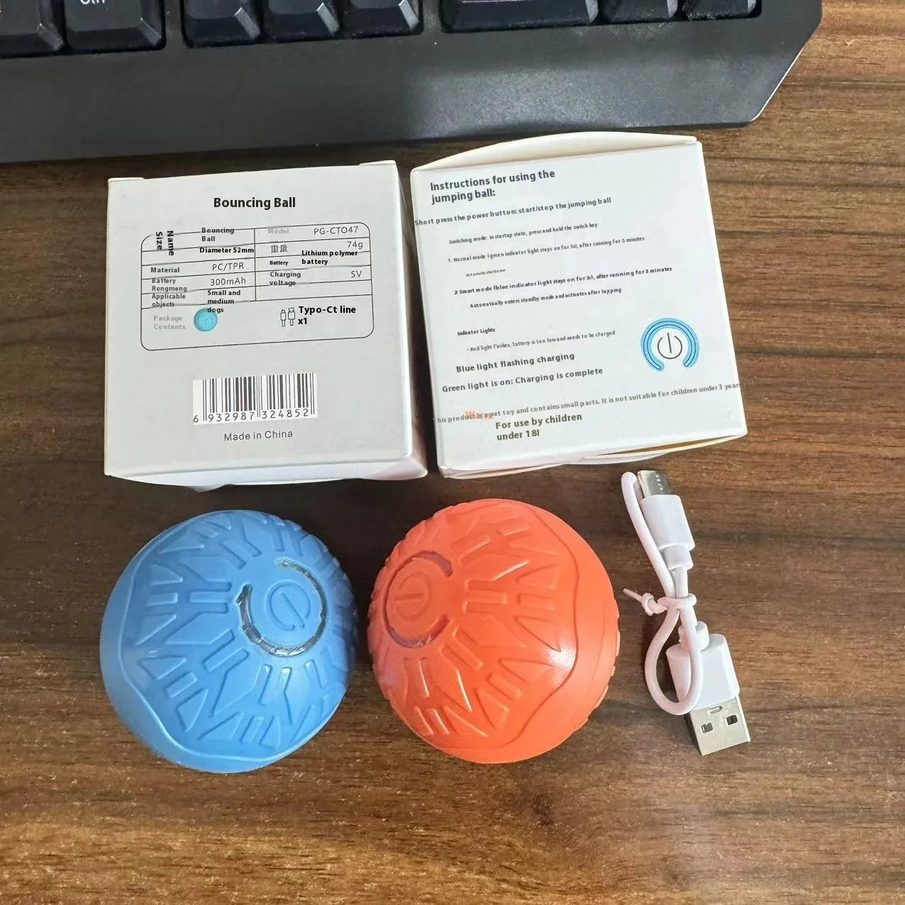 Blue and orange textured rubber bouncing balls with USB charging cable and packaging on wooden desk