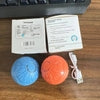Blue and orange textured rubber bouncing balls with USB charging cable and packaging on wooden desk