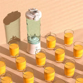 Portable blender with clear plastic jar, white base, surrounded by glasses of orange juice
